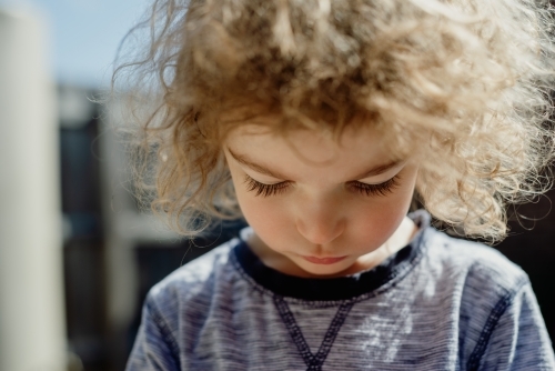 Closeup portrait of a young boy with messy curly hair looking down - Australian Stock Image