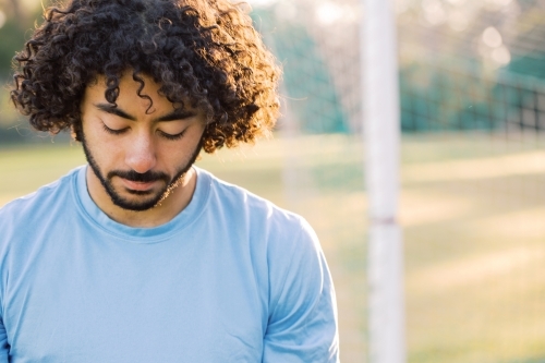 closeup shot of a man with curly hair and with beard looking down with blue shirt - Australian Stock Image