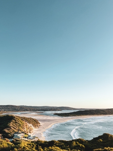 Coastal long shot of bay meeting river mouth with surf club buildings on beach - Australian Stock Image