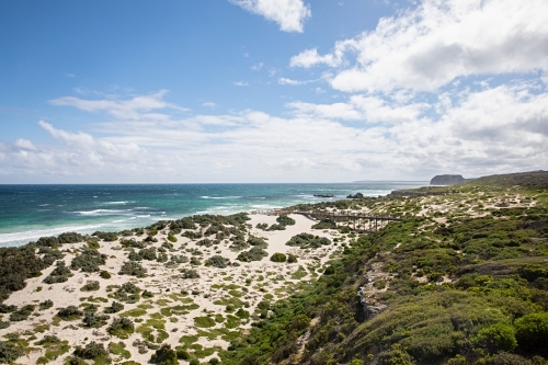 Coastal view with patches of grass and shrubs and a bridge leading to the shore - Australian Stock Image