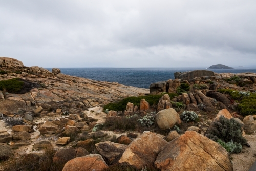 Colourful rocky foreshore on Southern Ocean with stormy sky and dark sea - Australian Stock Image