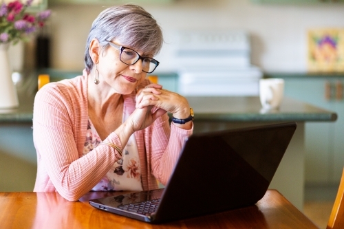 Confused woman looking at website on laptop in dining room - Australian Stock Image