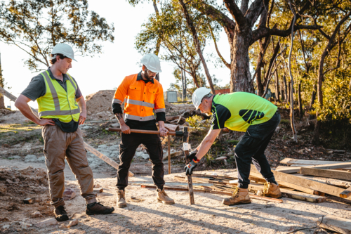 Construction workers driving a metal stake into the ground at construction site - Australian Stock Image