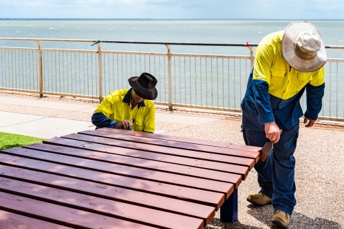 Council workers painting outdoor park benches and tables in Moreton Shire - Australian Stock Image