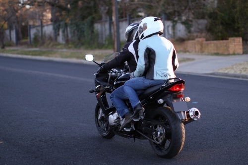 Couple riding a motorbike on a suburban street - Australian Stock Image