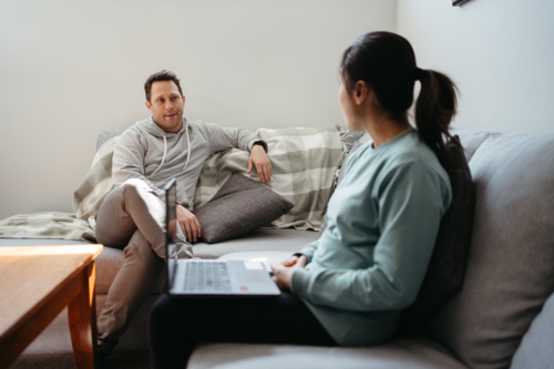 Couple talking while seated on the couch while woman holds a laptop - Australian Stock Image