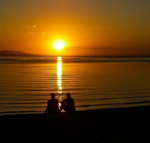 Couple watching the sunset over the water - Australian Stock Image