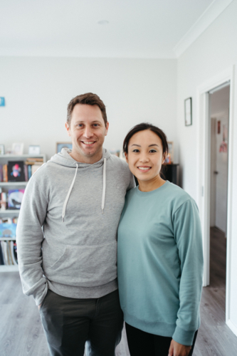 Couple wearing sweaters standing in their house living room. - Australian Stock Image