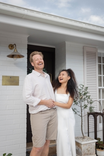 Couple wearing white standing together on front porch - Australian Stock Image