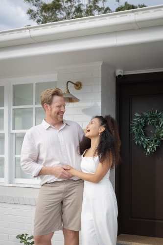 Couple wearing white standing together on front porch - Australian Stock Image