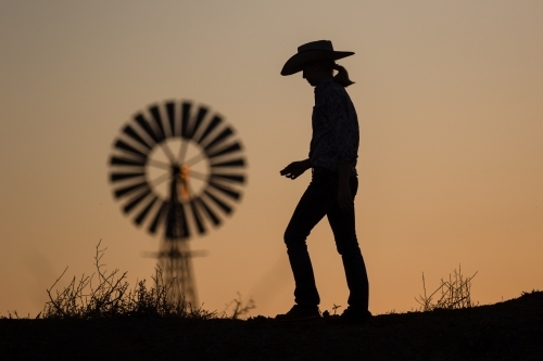 Cow girl and windmill at sunset - Australian Stock Image