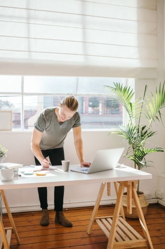 Creative employee standing over a desk while writing notes - Australian Stock Image