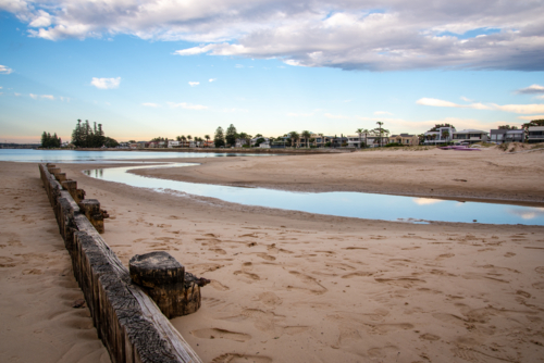 Creek flowing out to the bay past a wooden fence - Australian Stock Image