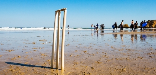 Cricket stumps on a beach with surfers in background - Australian Stock Image