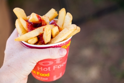 Cup of hot chips and tomato sauce held in hand at sports event - Australian Stock Image