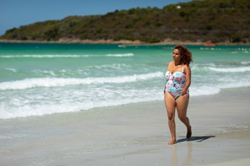 curvy woman walking along the shore on a sunny day - Australian Stock Image