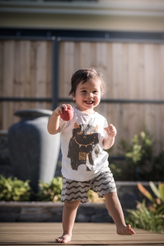 Cute 1 year old boy takes his first steps outside in his suburban backyard - Australian Stock Image