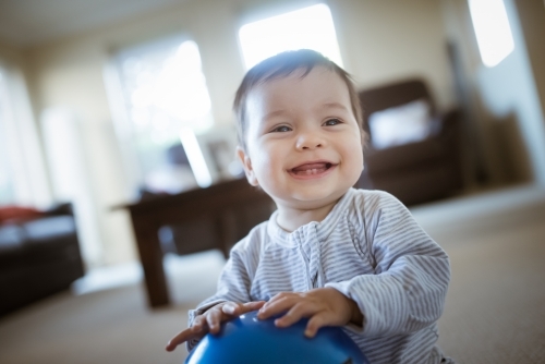 Cute 1 year old mixed race boy plays at home with a smiley face ball