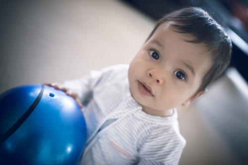 Cute 1 year old mixed race boy plays at home with a smiley face ball - Australian Stock Image