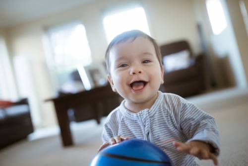 Cute 1 year old mixed race boy plays at home with a smiley face ball - Australian Stock Image