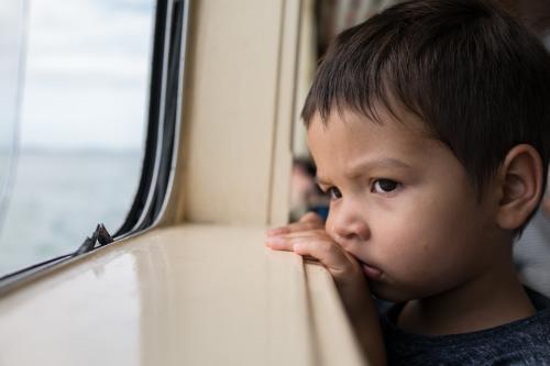 Cute 3 year old mixed race boy looks out a boat window - Australian Stock Image