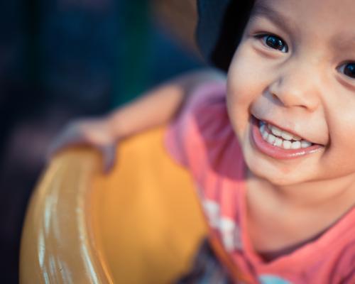 Cute 3 year old mixed race boy plays cheerfully on a playground slide - Australian Stock Image