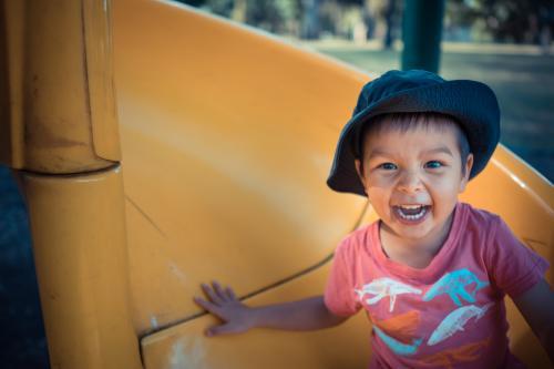 Cute 3 year old mixed race boy plays cheerfully on a playground slide - Australian Stock Image