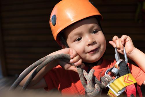 Cute 3 year old mixed race boy prepares to play on an adventure ropes course