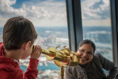 Cute 4 year old mixed race boy looks at his Asian mother with a telescope in Sydney Tower - Australian Stock Image