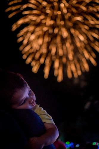 Cute mixed race baby boy cuddles his parent while new year's fireworks explode in background