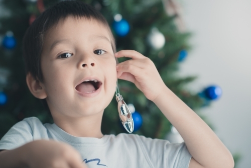 Cute mixed race boy hanging Christmas tree decorations on ear - Australian Stock Image