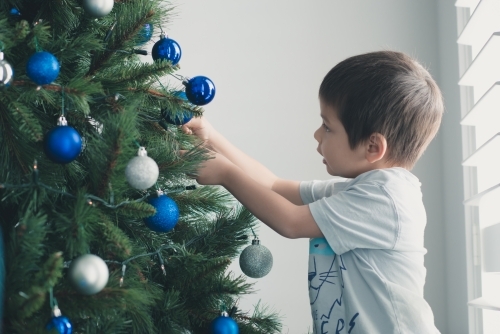 Cute mixed race boy hanging decorations on Christmas tree - Australian Stock Image