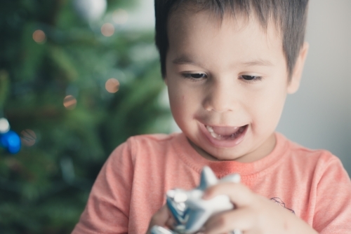 Cute mixed race boy hanging decorations on their Christmas tree - Australian Stock Image