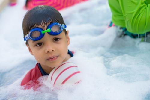 Cute mixed race boy plays in the bubbles of a backyard spa - Australian Stock Image