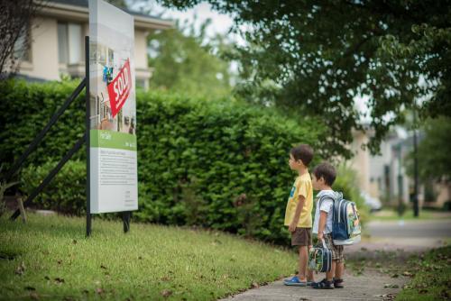 Cute mixed race brothers look at the sold sign in front of their suburban Sydney home - Australian Stock Image