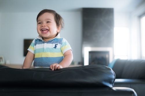Cute mixed race toddler plays on a black leather lounge at home