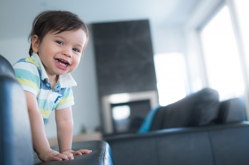 Cute mixed race toddler plays on a black leather lounge at home - Australian Stock Image