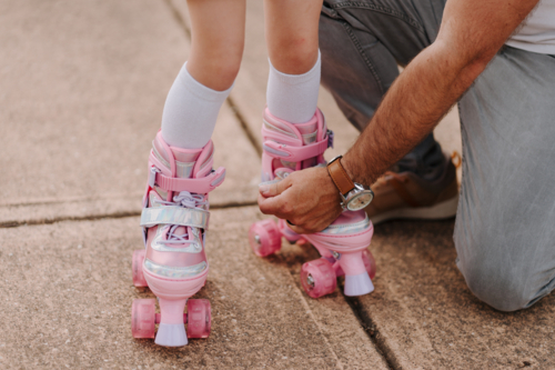 Dad helping daughter get into her roller blades. - Australian Stock Image