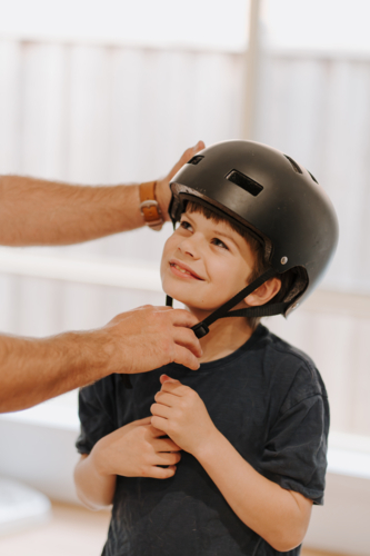 Dad helping his son put on his helmet. - Australian Stock Image