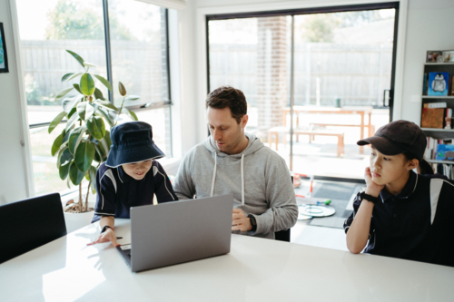 Dad helping kids with their homework using laptop. - Australian Stock Image