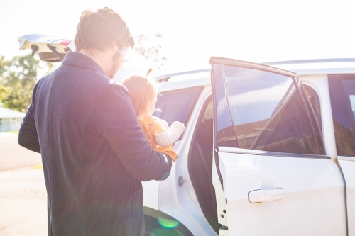 Dad putting baby girl in car with sun flare light - Australian Stock Image