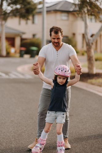 Dad teaching daughter how to roller skate. - Australian Stock Image