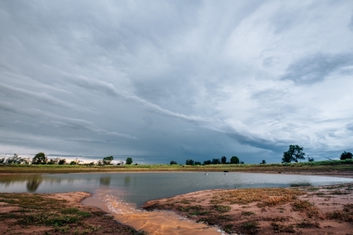 Dam with water running in against a stormy sky - Australian Stock Image