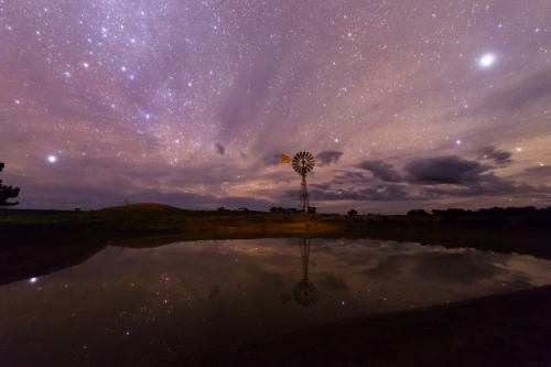 Dam with windmill at night under starry sky - Australian Stock Image