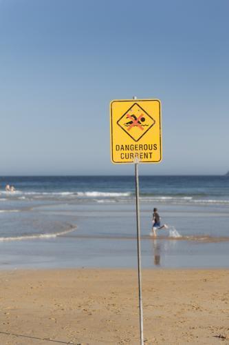 Dangerous Current Warning Sign on the Beach with Child Running In the Shallow Water - Australian Stock Image