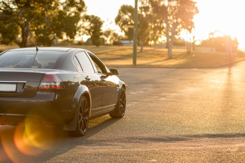 Dark car on quiet street driving into sunset with lens flare - Australian Stock Image