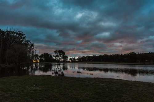 Dark cloudy night sky at sunset dusk reflecting on river water - Australian Stock Image