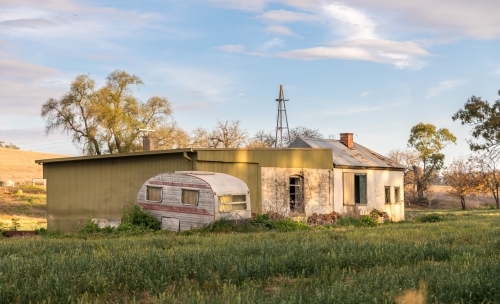 Derelict farm house with caravan out the back in the dappled sun lit evening - Australian Stock Image