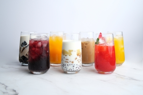 Different kinds of colorful juices in a tall glass served on a white marble countertop - Australian Stock Image