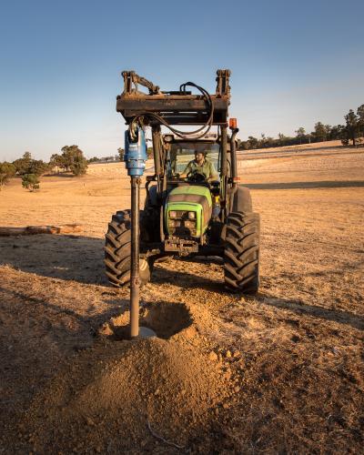 Digging a hole with hydraulic posthole digger on tractor - Australian Stock Image